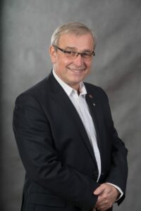 Dyrektor teatru w Elblągu Mirosław Siedler - postać przedstawiona na szarym tle, ubrany w białą koszulę i czarna marynarkę, posiada okulary.