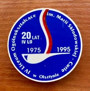 Znaczek IV LO na 20 lat funkcjonowania szkoły - niebieska kolorystyka z flagą Polski i napisem IV LO im. Marii Skłodowskiej-Curie w Olsztynie