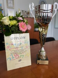 dyplom dla IV LO za zajęcie I miejsca w IV Drużynowych Mistrzostwach Powiatu Olsztyńskiego Szkół Ponadpodstawowych w Szachach o Puchar Przechodni Starosty Olsztyńskiego, Biskupiec 24 kwietnia 2023 r.; zdjęcie pucharu i kwiaty