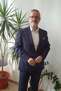 zastępca dyrektora Arkadiusz Biernat, w dłoni trzyma notes i długopis w tle kwiat