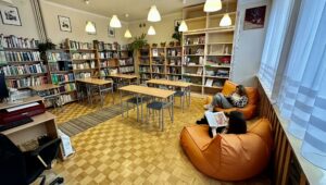 biblioteka szkolna w tle książki dwie uczennice siedzące na pomarańczowych pufach, czytają książki