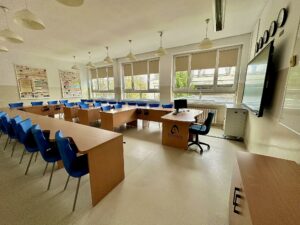 Cyfrowa szóstka - wzmocnienie kluczowych kompetencji uczniów poprzez doposażenie szkół na terenie Gminy Olsztyn sala lekcyjna niebieskie krzesła tablica multimedialna pięć zegarów tablice językowe na ścianach