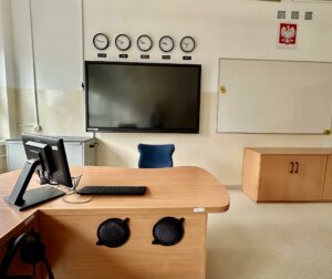sala lekcyjna niebieskie krzesła tablica multimedialna pięć zegarów tablice językowe na ścianach